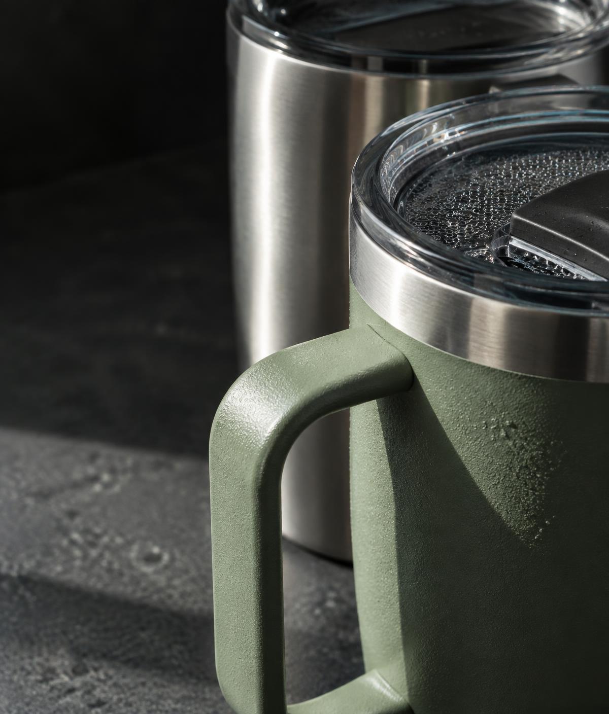 Close-up of a textured sage mug handle, brushed steel rim and droplets on the lid
