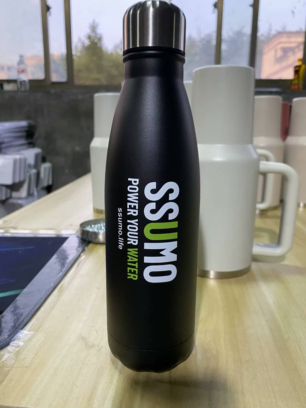 A real matte black cola bottle with the SSUMO Power Your Water logo on a worktable